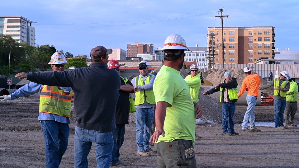 Construction workers stretch their arms on a job site before work begins for the day.